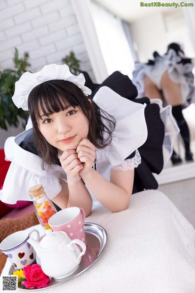 A woman in a maid outfit sitting at a table with a tray of tea.