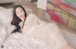 A woman in a white lingerie sitting on a white surface.