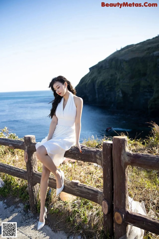 A woman in a white dress sitting on a wooden fence.