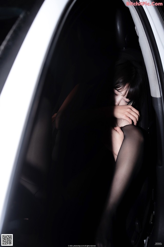 A woman sitting in the back seat of a car with her head in her hands.