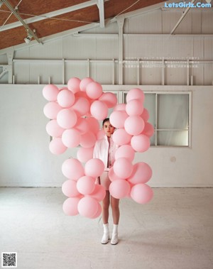 A woman in a pink jacket is surrounded by pink balloons.