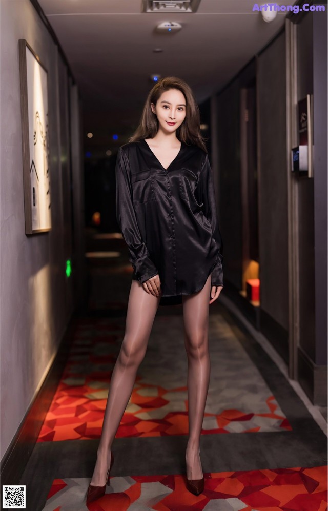 A woman in a black shirt and pantyhose posing in a hallway.