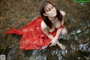 A woman in a red dress standing in front of a waterfall.