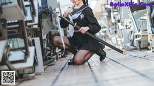 A woman sitting on the ground in front of a bunch of guns.