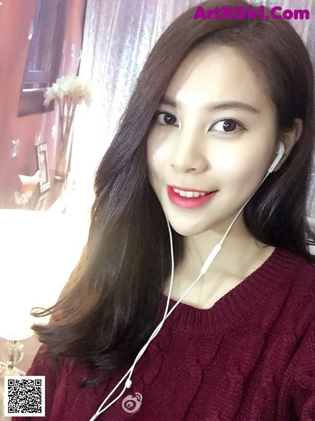 A woman wearing a red sweater and ear buds.