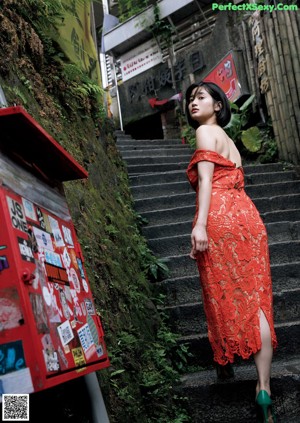 A woman in a red dress leaning against a wall.