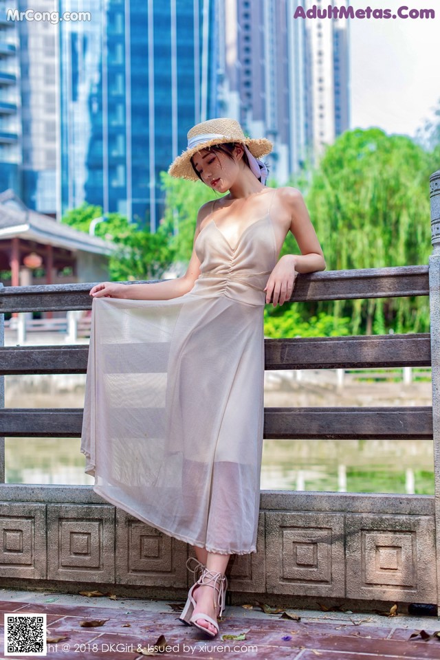 A woman in a dress and hat leaning against a fence.