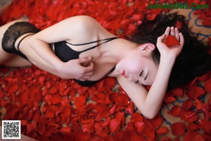 A woman in a black lingerie laying on a bed of rose petals.
