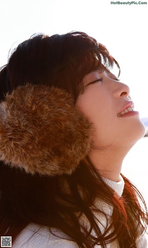 A young woman wearing a fur hat sitting on the ground.