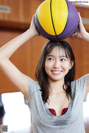 A woman is sitting on a basketball on the floor.