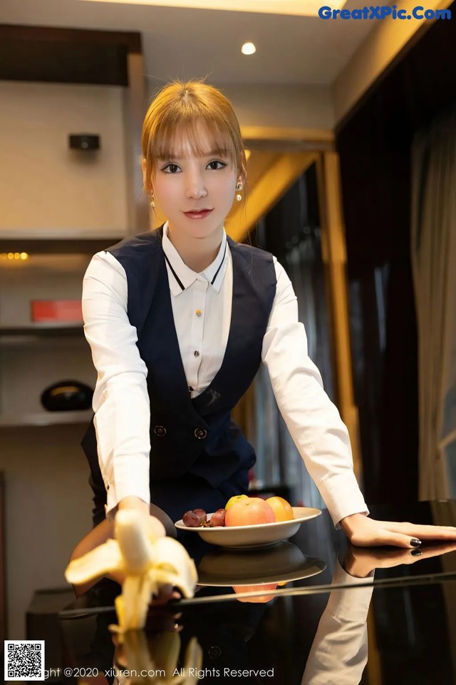 A woman holding a plate of fruit on a table.