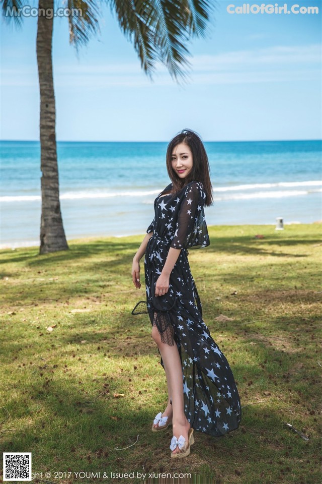 A woman in a black dress standing on a grassy field next to the ocean.