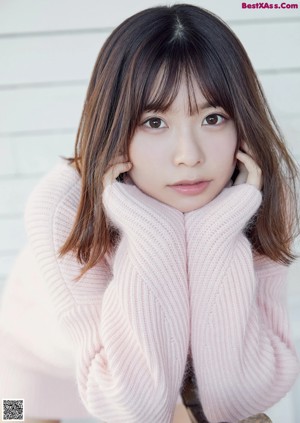 A woman sitting on a bed in a pink sweater.