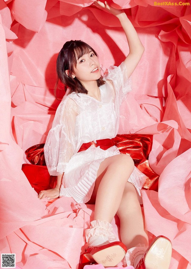 A woman in a white dress and red shoes sitting on a pile of pink paper.