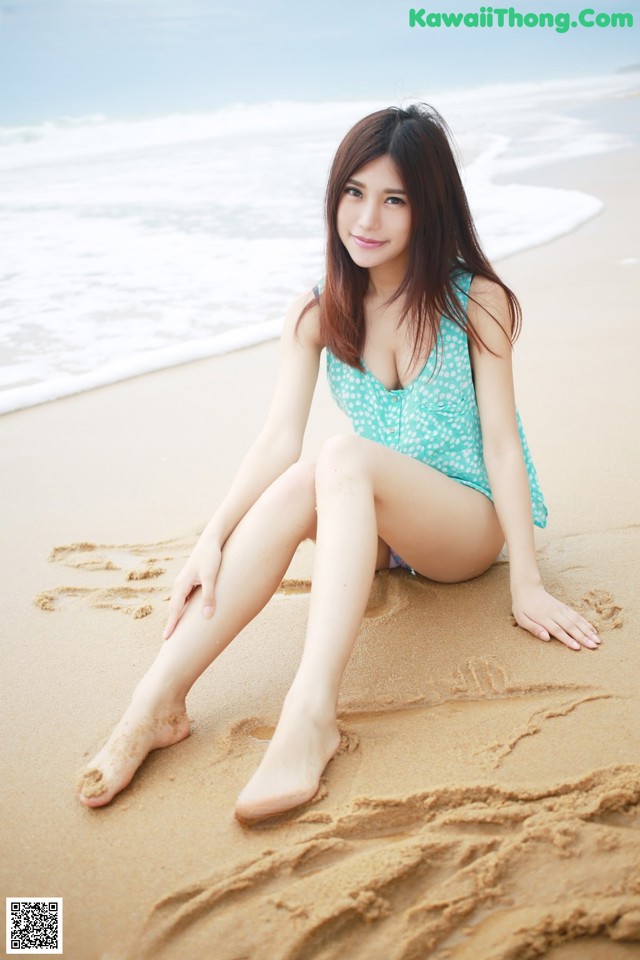 A woman in a blue bathing suit sitting on the beach.