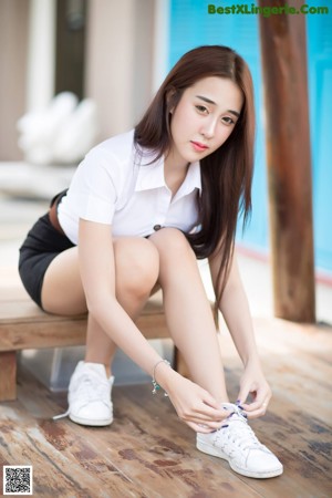 A woman sitting on a wooden bench with her legs crossed.