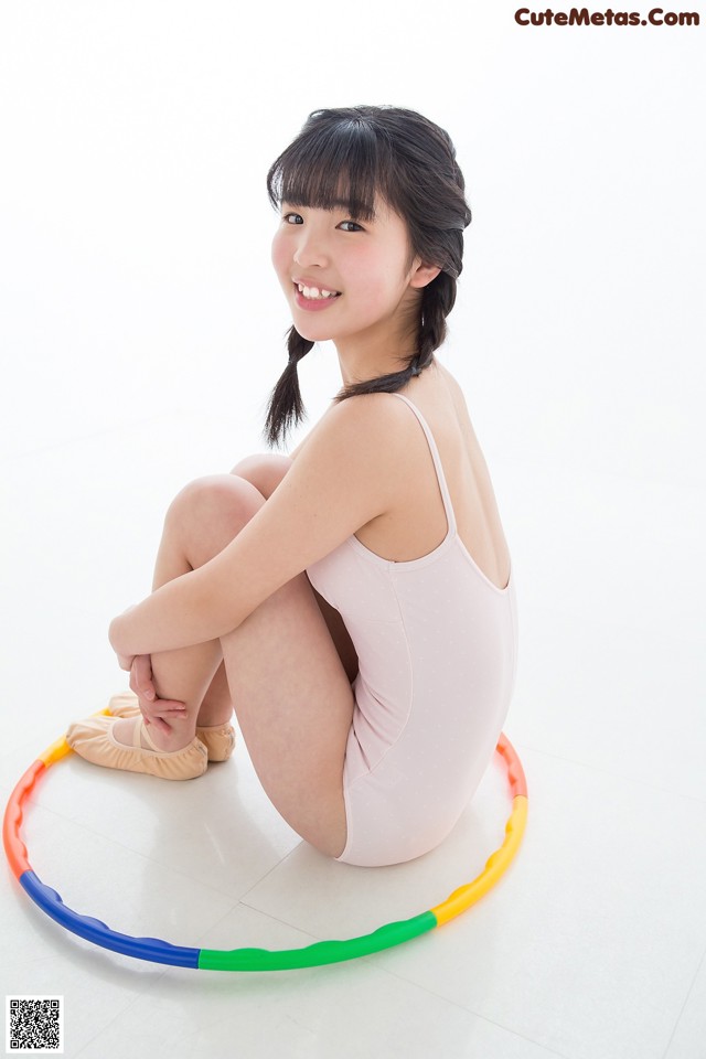 A young woman sitting on the floor with a hula hoop.