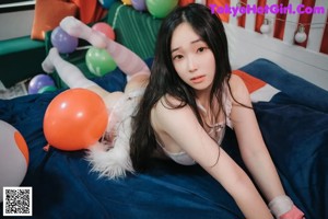 A woman in a white lingerie sitting on a bed with balloons.