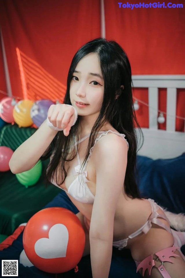 A woman in lingerie sitting on a bed with balloons.