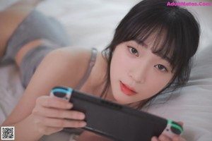 A woman laying on a bed next to a Nintendo Switch.