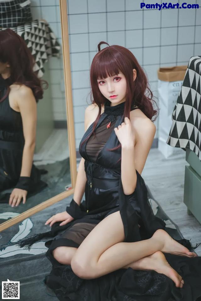 A woman in a black dress sitting on a bed.