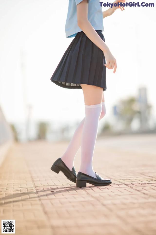 A woman in a blue shirt and black skirt is walking down a sidewalk.