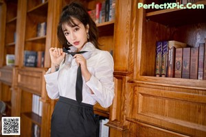 A woman in a white shirt and black skirt posing in front of a desk.