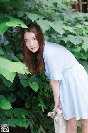 A woman in a blue and white striped shirt leaning against a bamboo fence.