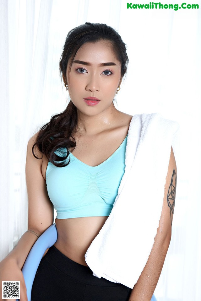 A woman in a blue top and black leggings holding a towel.