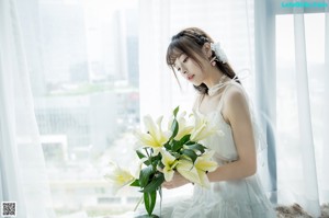 A woman in a white dress holding a bunch of white flowers.