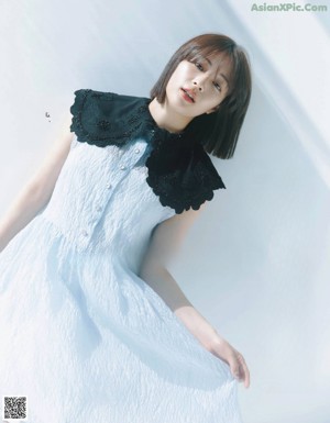 A woman in a blue dress standing in front of a white background.
