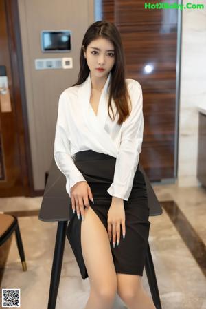 A woman in a white shirt and black skirt sitting on a table.