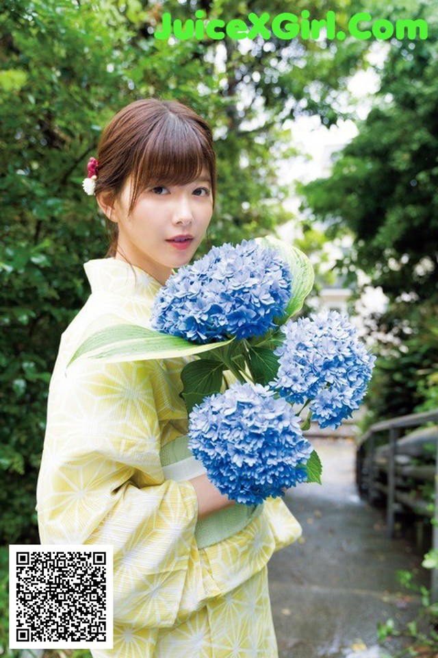 A woman in a yellow kimono holding a bunch of blue flowers.