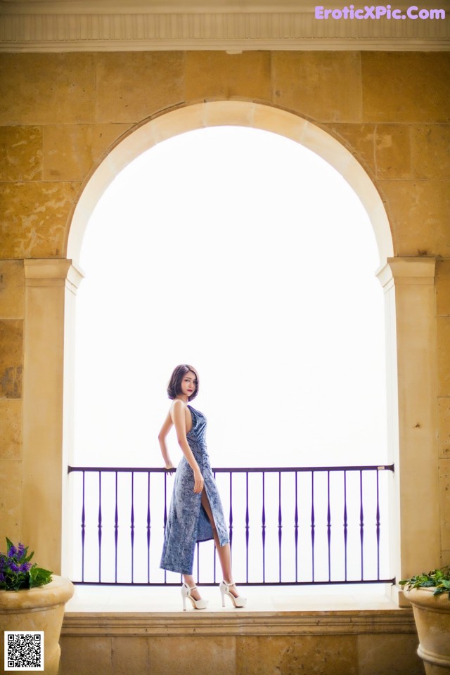 A woman in a blue dress standing on a balcony.