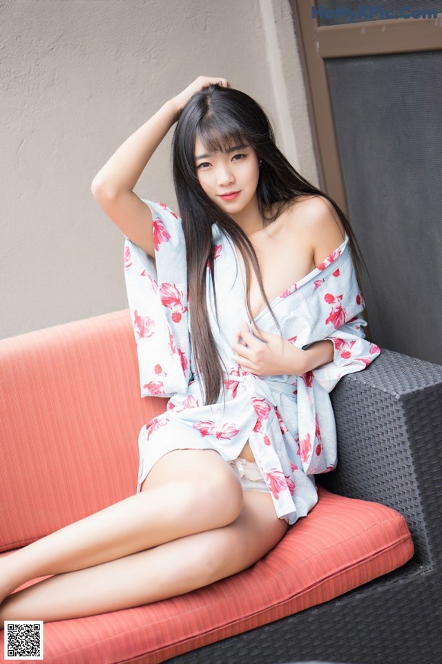 A woman sitting on a red couch wearing a blue and white robe.