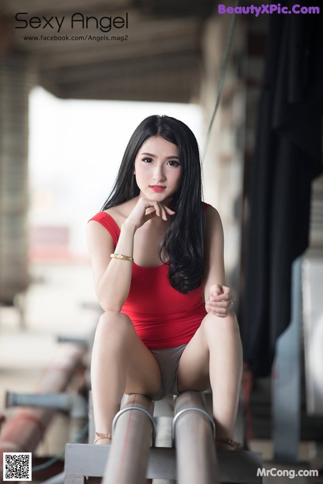 A woman in a red top sitting on a metal pole.